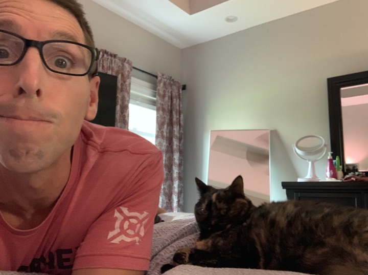 Chris lying beside Annie, a tortoiseshell cat, on a bed.